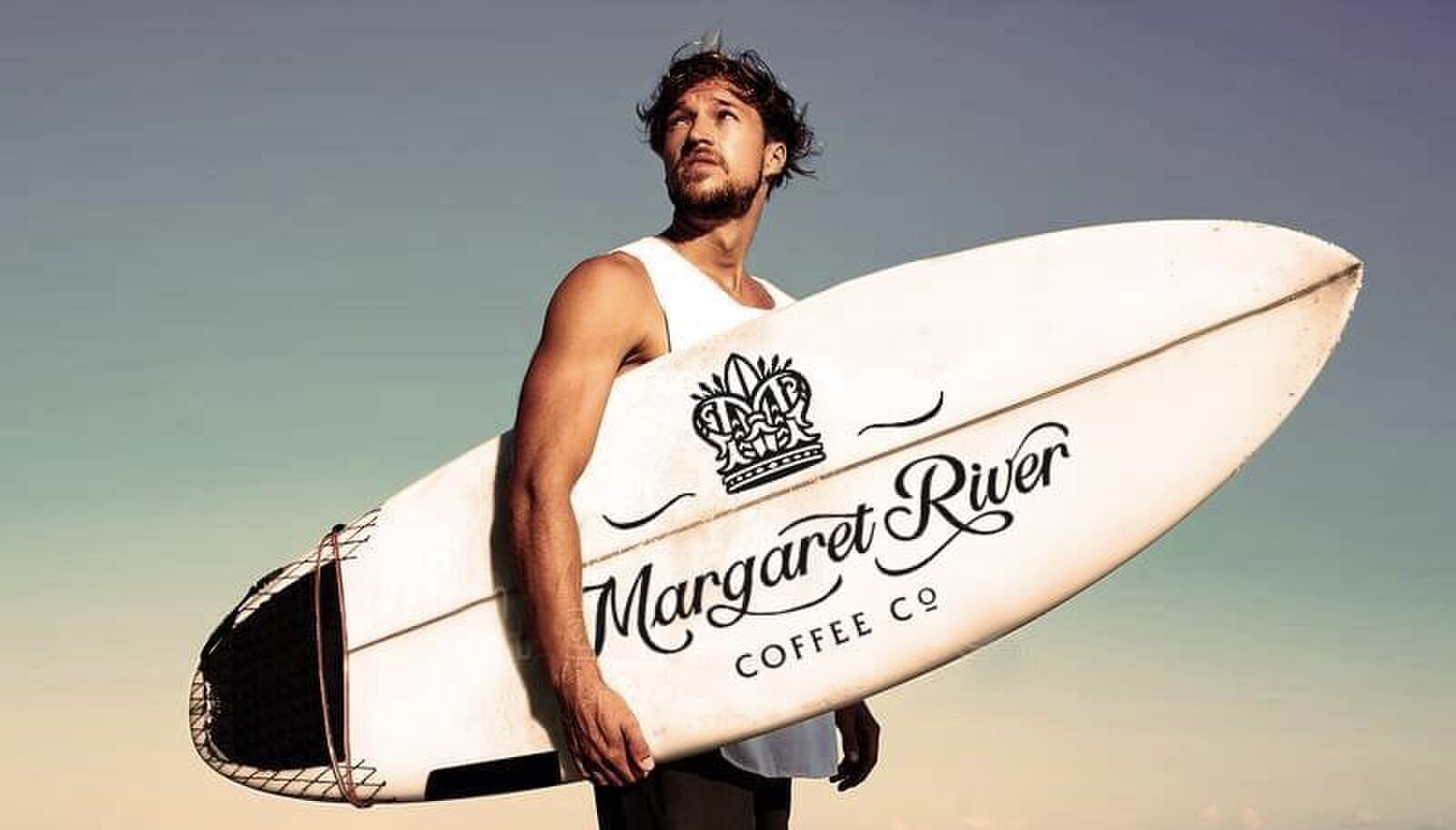 A surfer carrying a Margaret River Coffee Co branded surfboard
